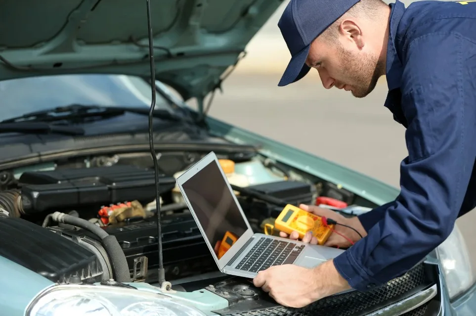 Auto mechanic using a laptop and diagnostic tool under an open car hood to troubleshoot vehicle issues, representing car inspection or repair services, lemonmyvehicle