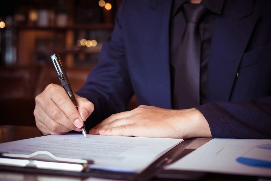 Close-up of a lawyer in a suit signing a legal document on a clipboard, symbolizing contract agreements or legal paperwork, lemonmyvehicle
