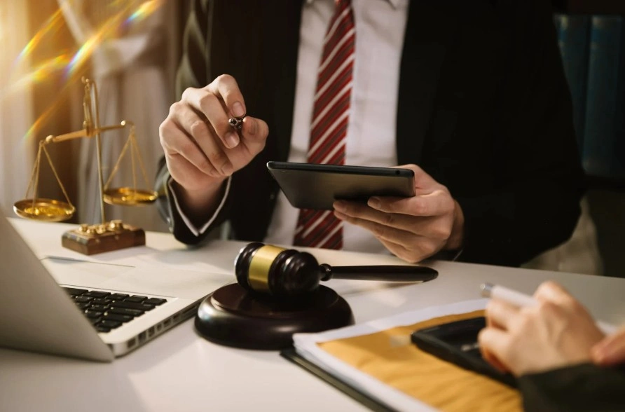 Lawyer in a suit using a tablet, with legal scales, a gavel, and documents on the desk, symbolizing legal consultation or car law disputes, lemonmyvehicle