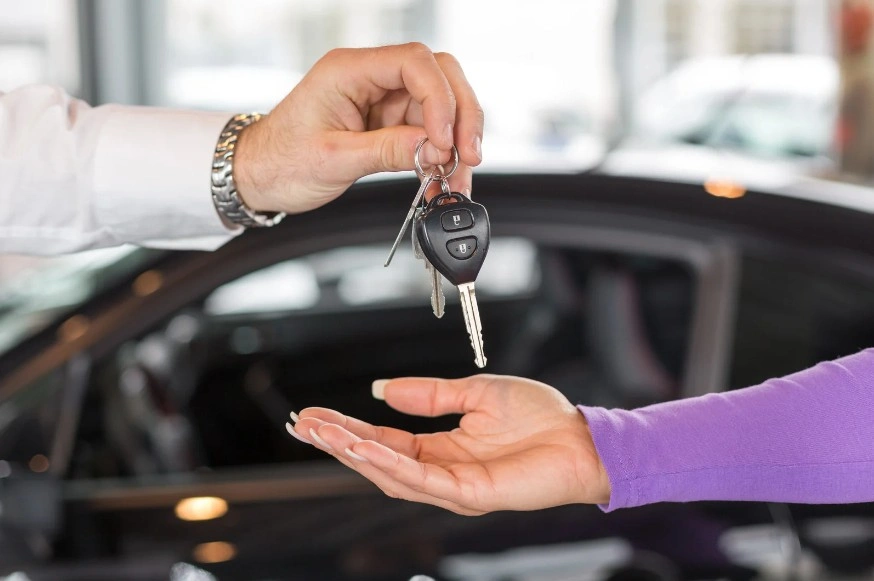 Person handing over car keys to a buyer inside a dealership, symbolizing vehicle purchase, leasing, or car ownership transfer, lemonmyvehicle