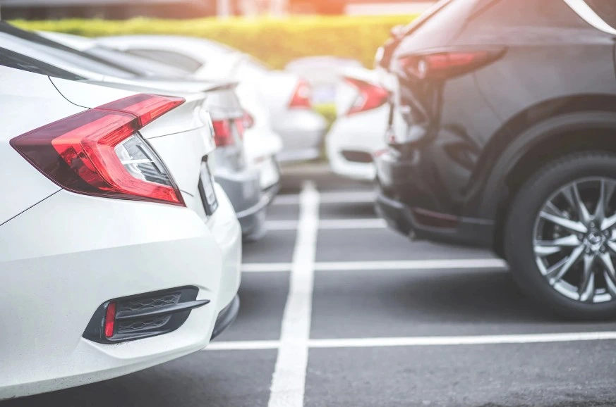 Rear view of parked cars in a parking lot, featuring modern sedans and SUVs with a blurred urban background, lemonmyvehicle