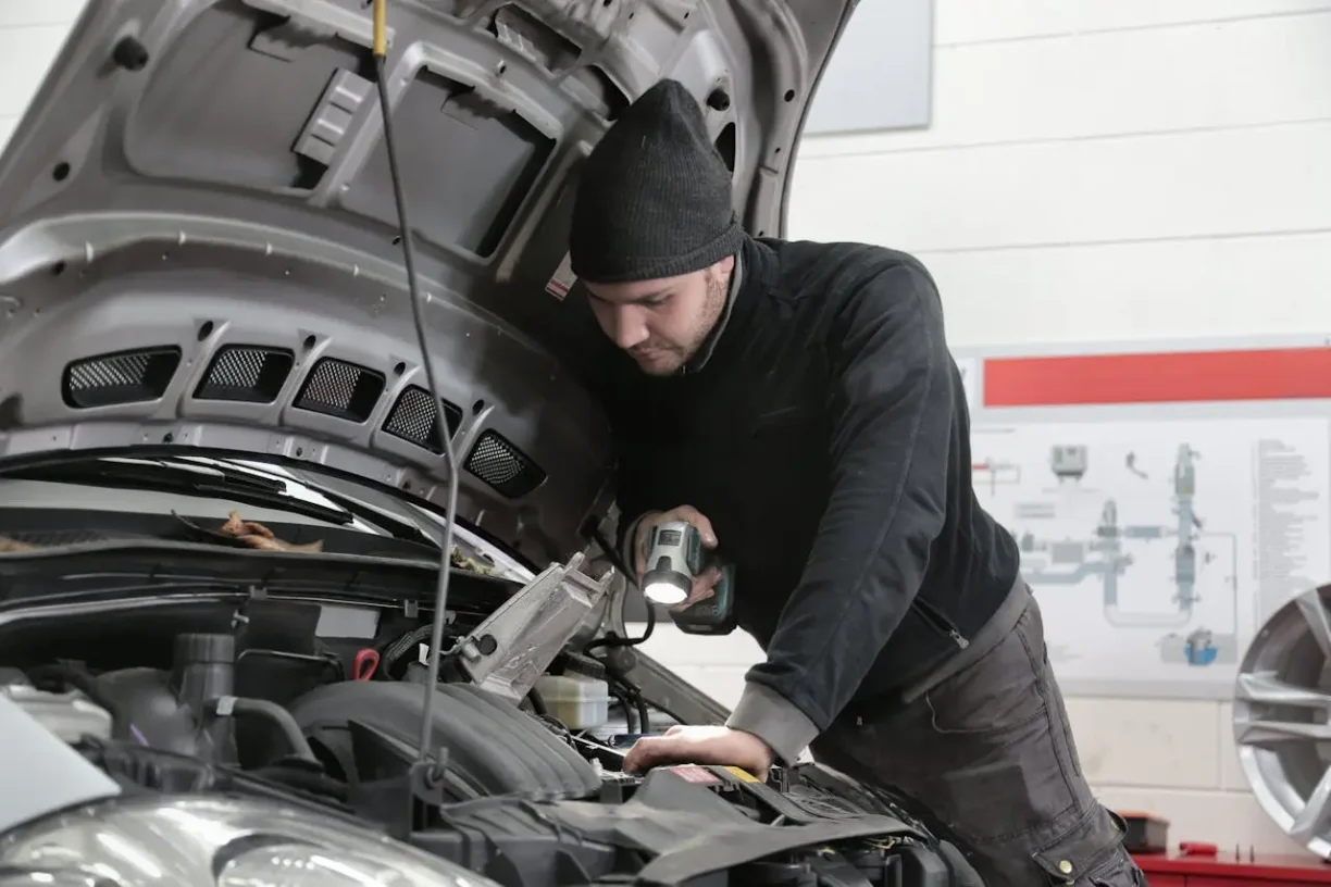 Auto mechanic inspecting engine under open hood with flashlight in garage, lemonmyvehicle