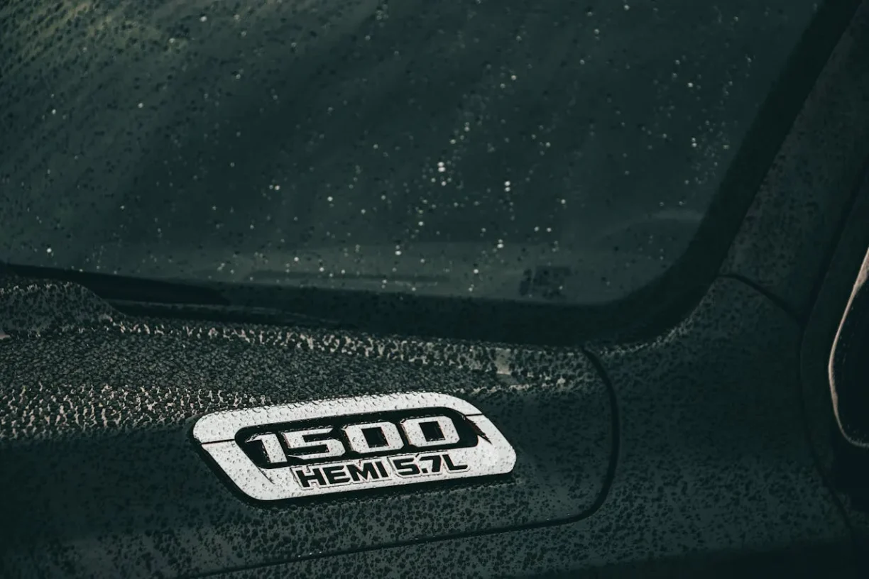 Close-up of 1500 HEMI 5.7L badge on a rain-drenched vehicle hood, lemonmyvehicle