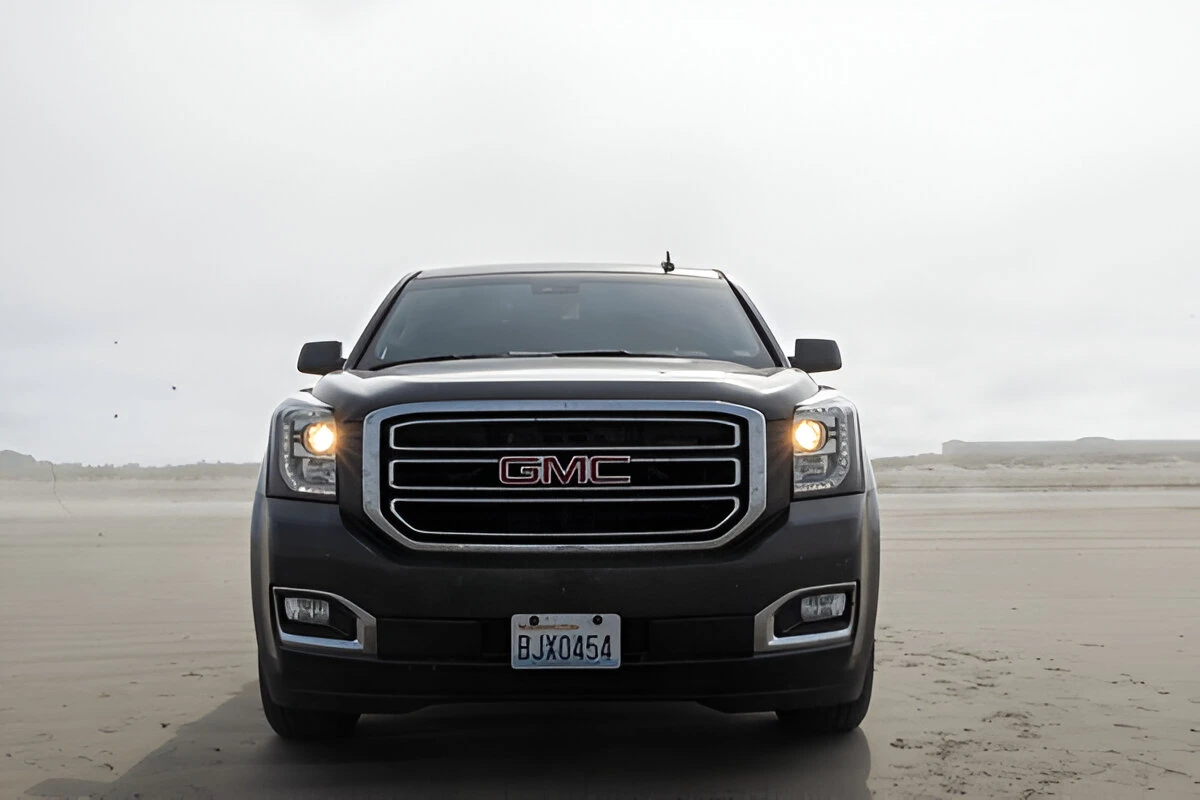 Front view of a black GMC SUV with headlights on, parked on a beach, lemonmyvehicle