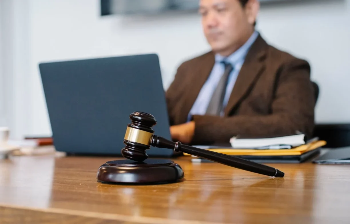 Gavel on a wooden desk with a person in a suit working on a laptop in the blurred background, symbolizing legal services, lemonmyvehicle
