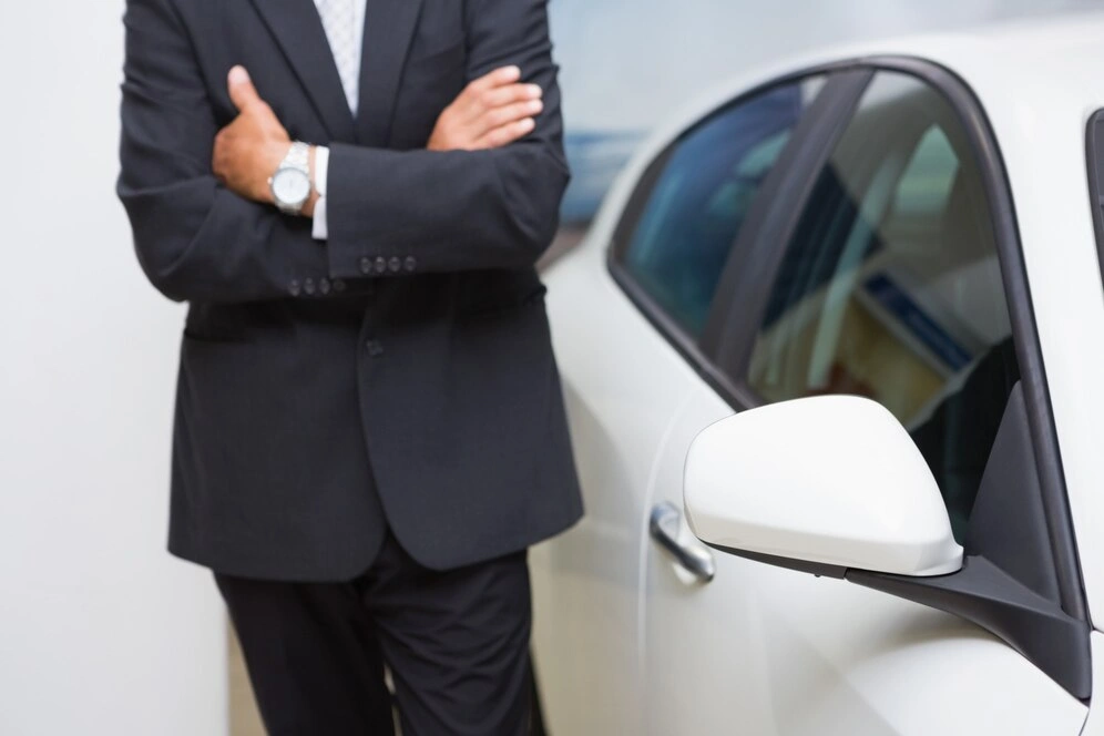 Lawyer in suit standing confidently with arms crossed by car, lemonmyvehicle