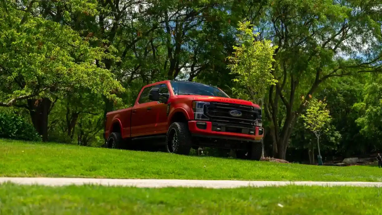 Red Ford F-250 Super Duty pickup truck parked on a grassy hill with trees in the background, lemonmyvehicle