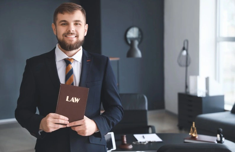 Smiling lawyer in a suit holding a law book in a modern office, lemonmyvehicle