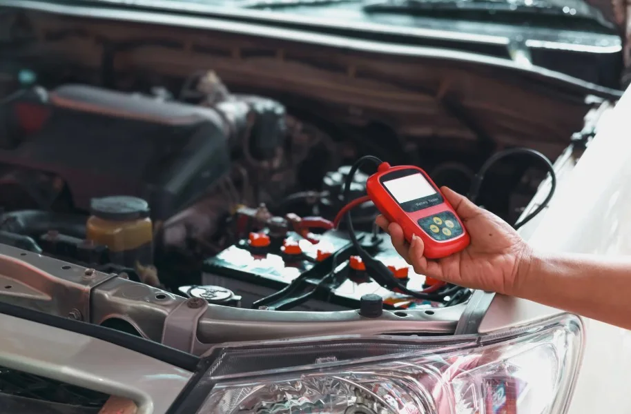 A hand using a diagnostic tool on a car battery, representing vehicle problems and the need for inspection in Lemon Law cases.
