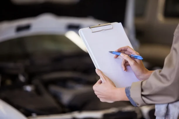 Inspector holding clipboard while examining car engine for defects