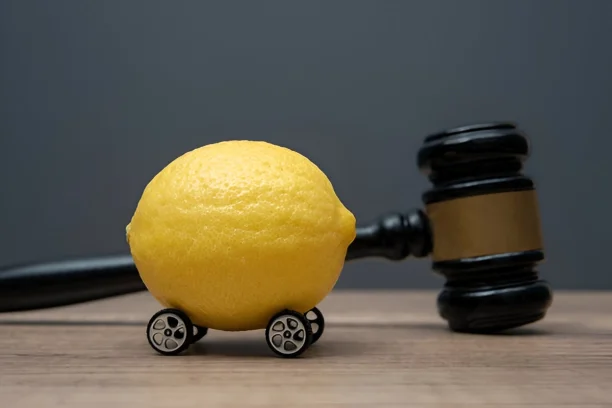 Lemon with wheels beside judge gavel symbolizing lemon law for defective cars