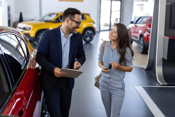 Car dealer and buyer smiling while discussing a new vehicle in the showroom.