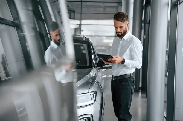 Car dealer reviewing inspection details on tablet beside vehicle, lemonmyvehicle