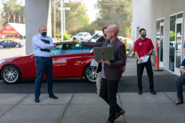 Car dealership staff discussing sales strategy outside showroom.