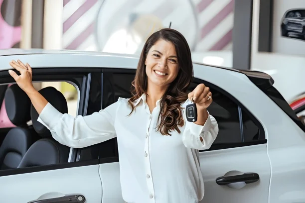 Happy woman holding car keys beside her new car, showing successful purchase.