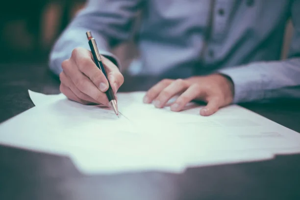 Man signing car purchase or lease agreement paperwork at desk.