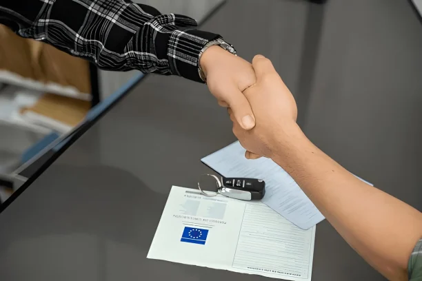 Two people shaking hands over car documents and keys, representing a completed vehicle sale under fair Lemon Law terms.
