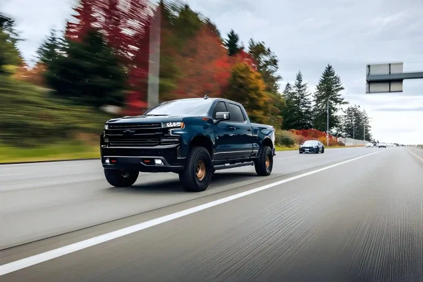 Black Chevrolet pickup truck driving on an open highway with autumn trees in the background.