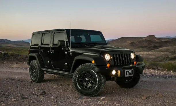 Black Jeep SUV parked on rocky terrain during sunset with mountain view.