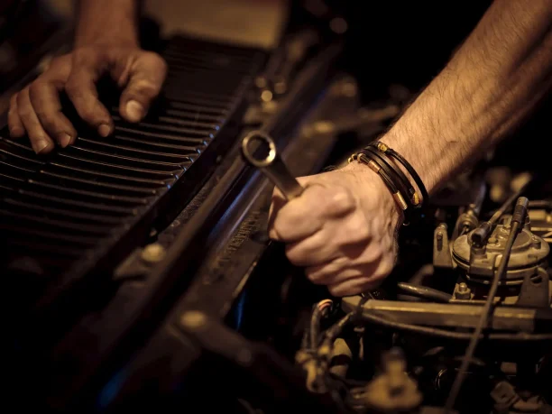 Mechanic using wrench to repair car engine in dimly lit garage.