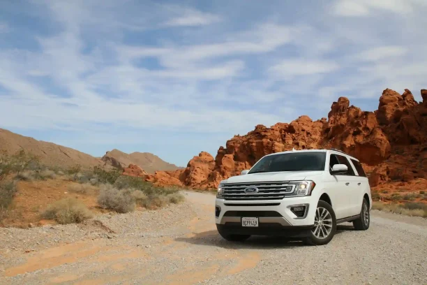 White Ford SUV driving on a desert road with red rock formations.