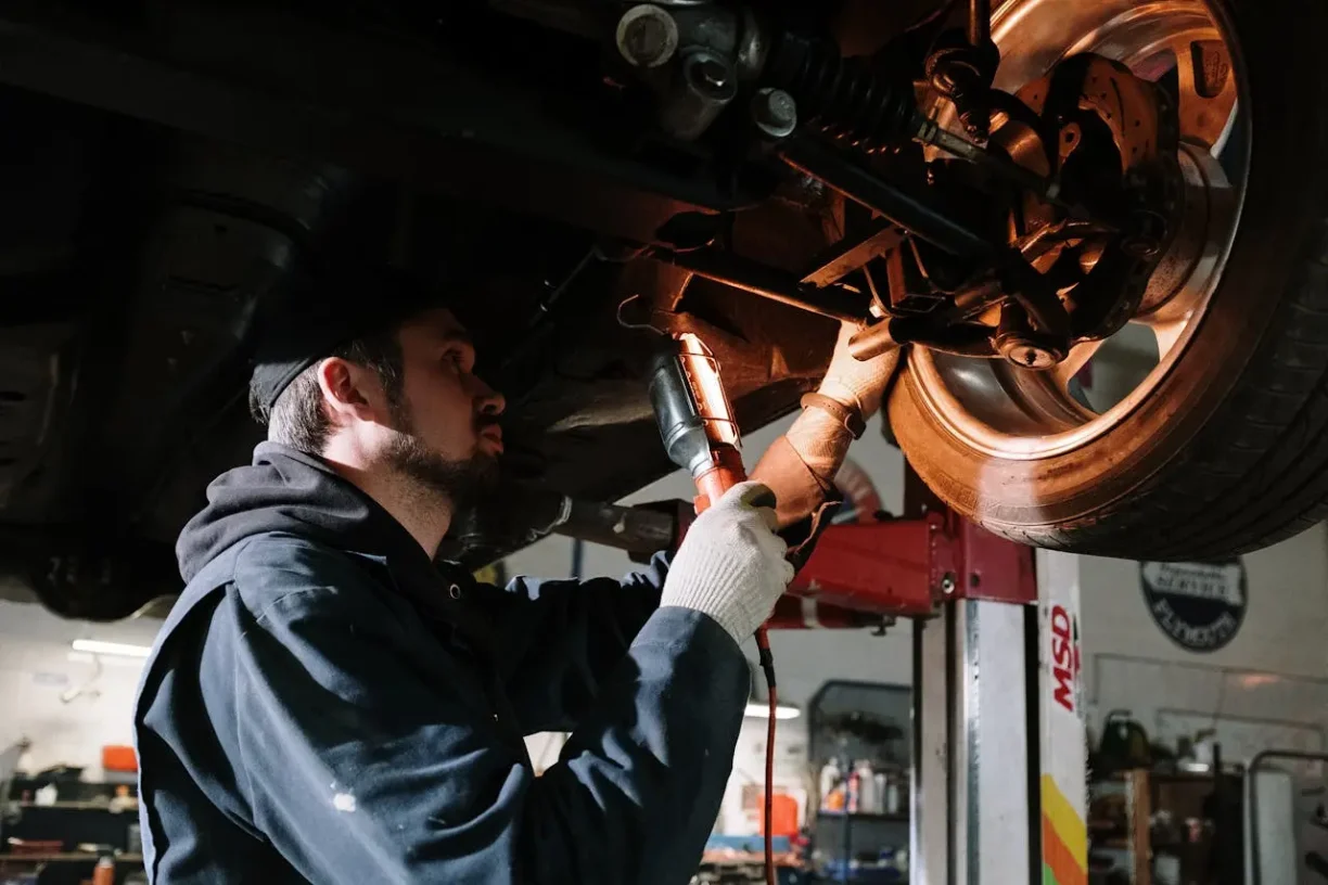 Auto mechanic using power tools to repair suspension under a lifted vehicle