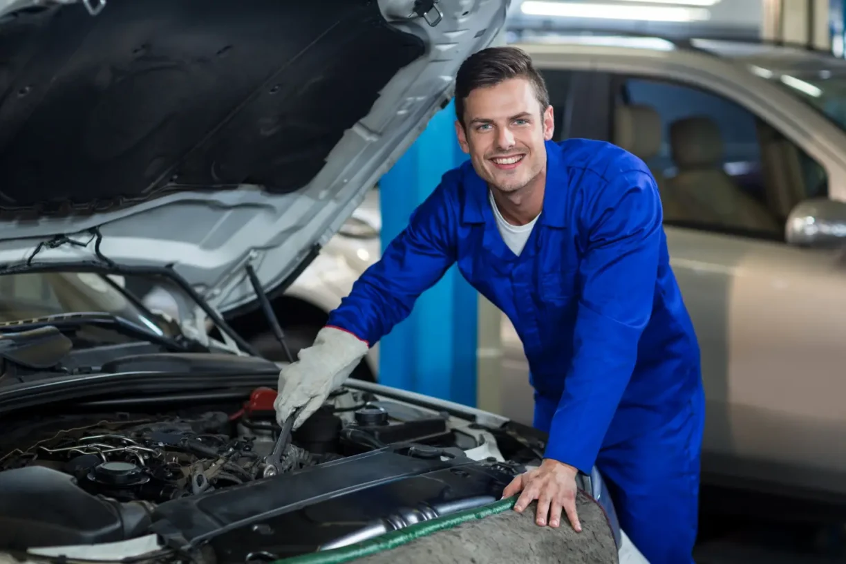 Professional auto mechanic smiling while inspecting a car engine in a repair shop, highlighting vehicle diagnostics, maintenance, and expert automotive service.