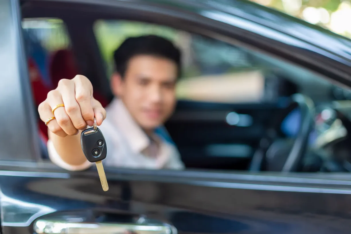 Happy car buyer holding vehicle keys while sitting inside a newly purchased car.
